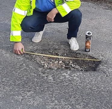man wearing a high viz jacket measuring a pothole on a road