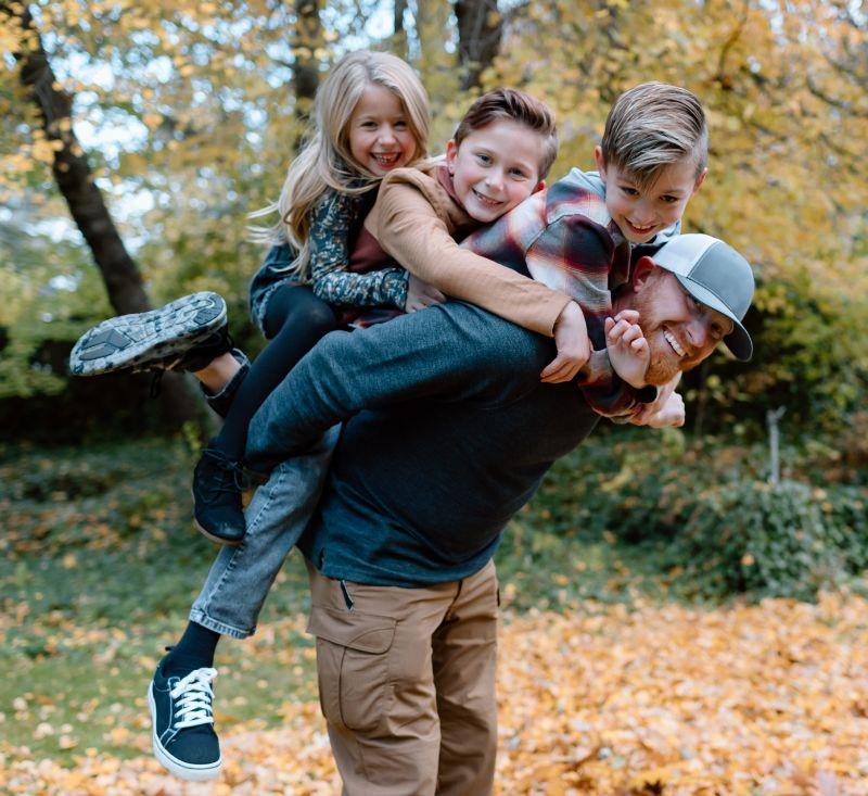 Man with three young children on his back all are smiling